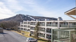 A multi-story residential building with balconies, a parking area, and a view of a hilly landscape in the background. - Ski Condo on Beech Mountain (Beech Mountain)