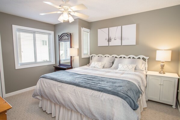 A bedroom with a bed, nightstands, a ceiling fan, and a large window.