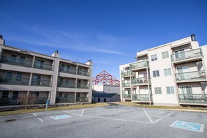 A multi-story residential building with balconies, a parking lot with handicapped parking spaces, and a red structure in the background.