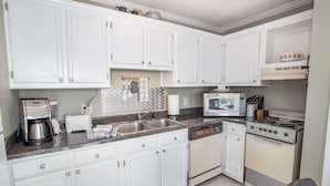A compact kitchen with white cabinets, a built-in microwave, a stove, and a coffee maker. - Ski Condo on Beech Mountain (Beech Mountain)