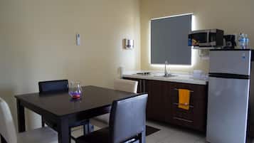 A compact kitchen with a dining table, chairs, a refrigerator, a microwave, and a coffee maker.