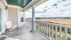 A covered porch with white rocking chairs, a view of a marshy landscape, and a clear sky.