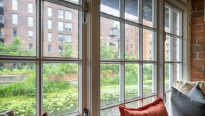A room with large windows, a view of a brick building, and a glimpse of a garden with water lilies.