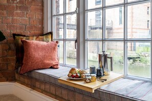 Relax in a serene courtyard view from this cozy seating area, complete with a bench and a tray of sweet treats.