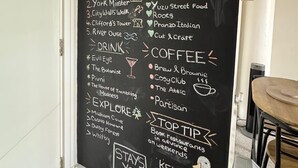 A chalkboard sign in a room with a door and a plant, listing local eateries and coffee shops.