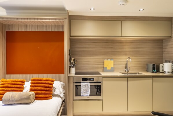 Une chambre d’hôtel moderne avec un lit, une kitchenette et un grand mur orange.