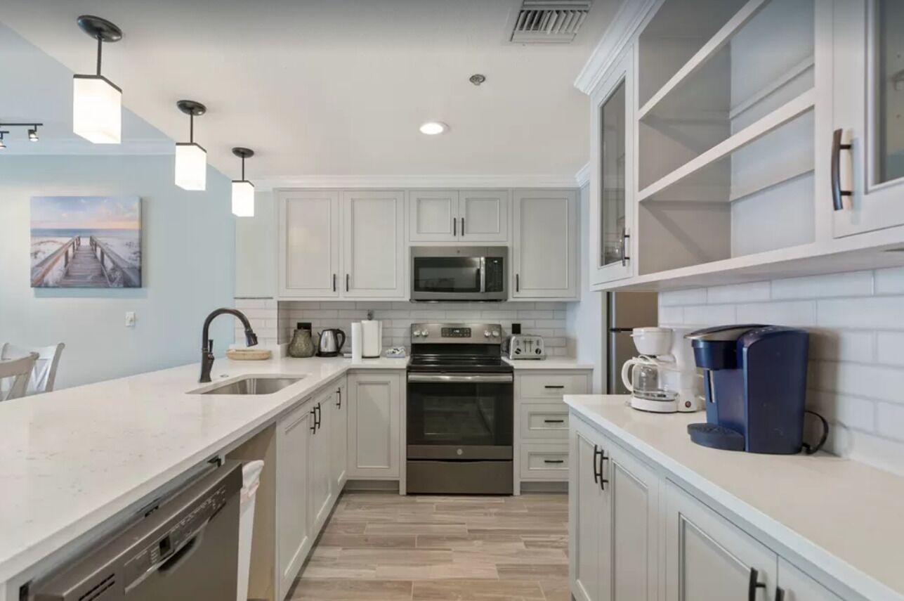 A modern kitchen with white cabinetry, stainless steel appliances, and pendant lighting.
