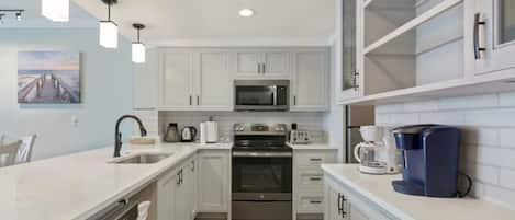 A modern kitchen with white cabinetry, stainless steel appliances, and pendant lighting.