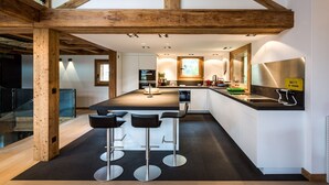 A modern kitchen with a central island, bar stools, and wooden beams. - Chalet Rass: Sublime five bedroom chalet fully equipped (Chamonix)
