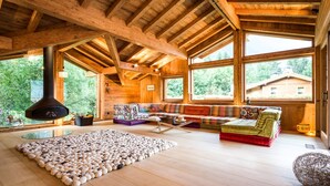A spacious cabin with high ceilings, large windows, a cozy seating area with a colorful sofa, and a unique rug made of eggshells. - Chalet Rass: Sublime five bedroom chalet fully equipped (Chamonix)