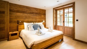 A bedroom with a wooden headboard, a large window, and a wooden floor. - Chalet Rass: Sublime five bedroom chalet fully equipped (Chamonix)
