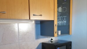 A compact kitchen with wooden cabinets, a built-in microwave, a sink with a drying rack, and a front-loading washing machine.