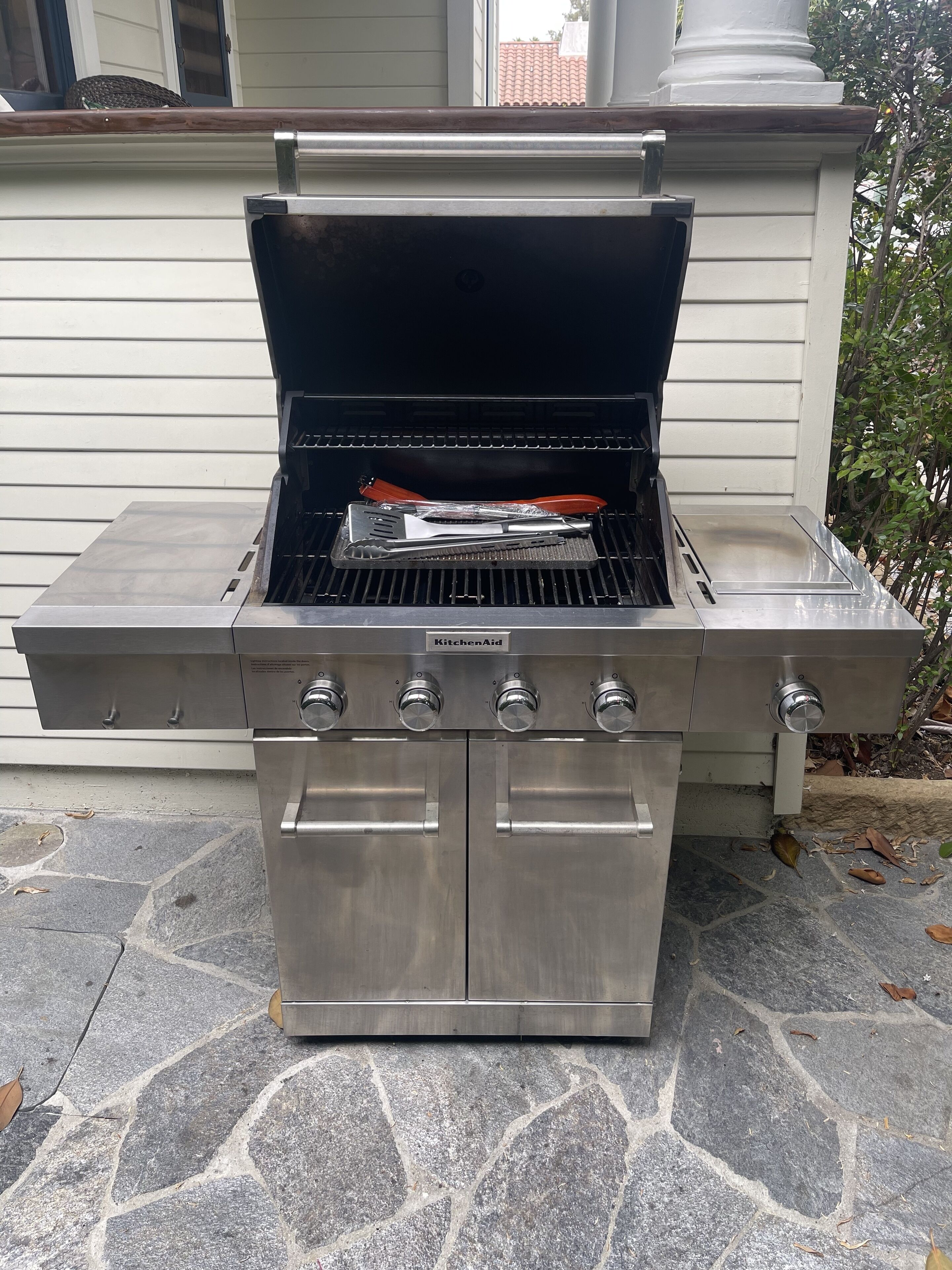 En utomhusgrill i rostfritt stål med fyra brännare, en sidohylla och ett lock som kan öppnas och stängas.