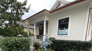 Een woonhuis met een veranda, een standbeeld en een tuin met verschillende planten en bloemen.