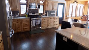 A modern kitchen with wooden cabinets, a stainless steel stove, and a large island with a sink. - Beautiful 4 BDRM Retreat on Loon Lake with Sauna and Sand Beach! (Cohasset)