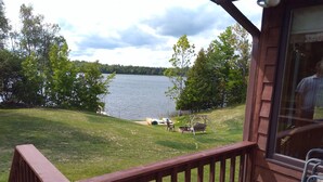 A deck with a view of a lake, surrounded by trees and a grassy area with outdoor furniture. - Beautiful 4 BDRM Retreat on Loon Lake with Sauna and Sand Beach! (Cohasset)