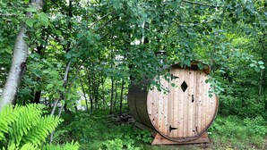 A wooden structure with a door, surrounded by dense green foliage. - Beautiful 4 BDRM Retreat on Loon Lake with Sauna and Sand Beach! (Cohasset)
