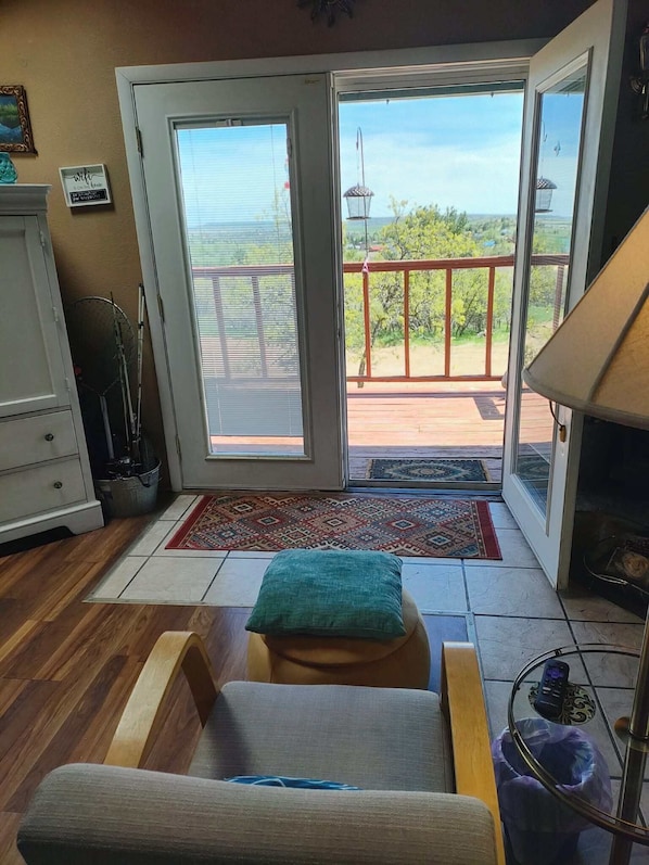 A room with a sliding glass door leading to a balcony, a small sofa, a lamp, and a trash bin.