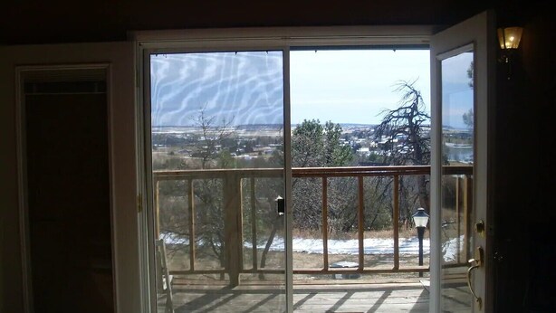Une porte-fenêtre coulissante donnant sur un balcon d’où l’on peut admirer un paysage enneigé et des arbres.