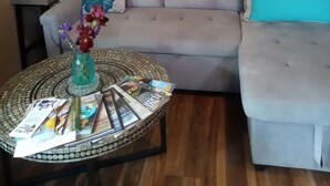 Un salon avec un canapé gris, une table basse ronde sur laquelle sont posés des magazines, un vase avec des fleurs et des œuvres d'art abstraites accrochées au mur.