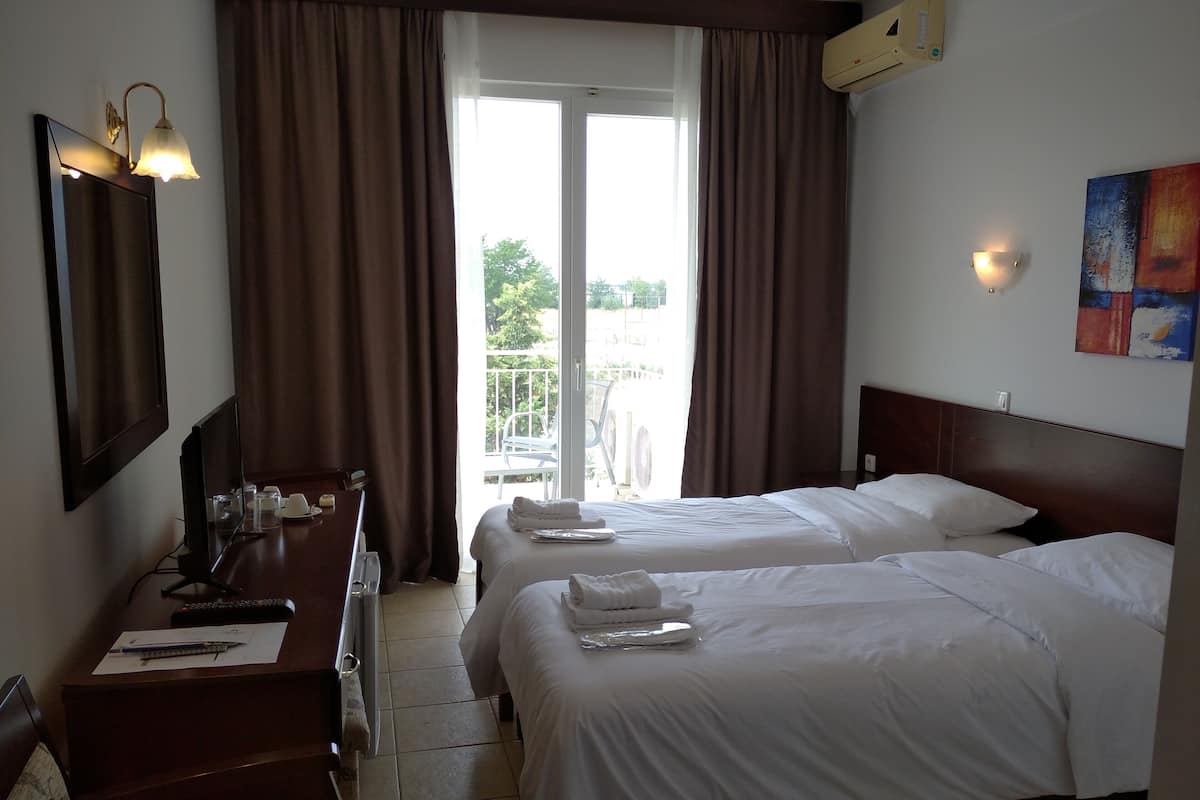 A hotel room with two beds, a desk with a computer, a mirror, and a window with curtains.