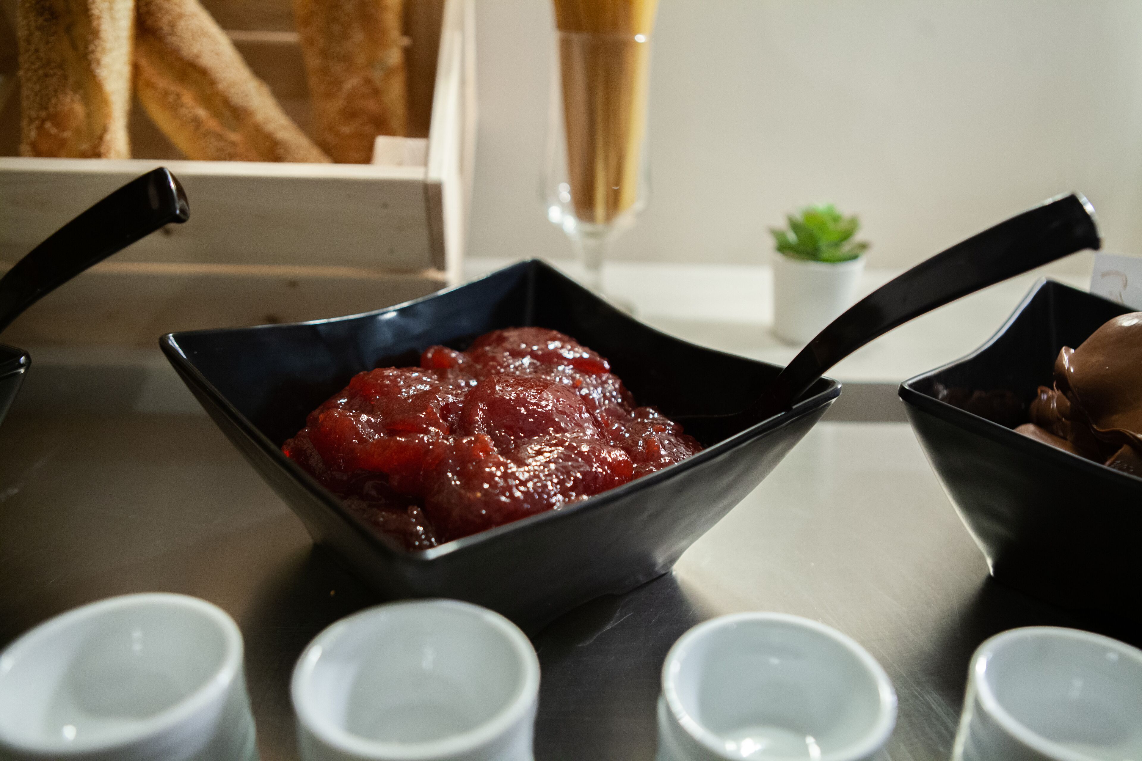 A kitchen counter with a black bowl containing a red fruit compote, a knife, and several small white cups.