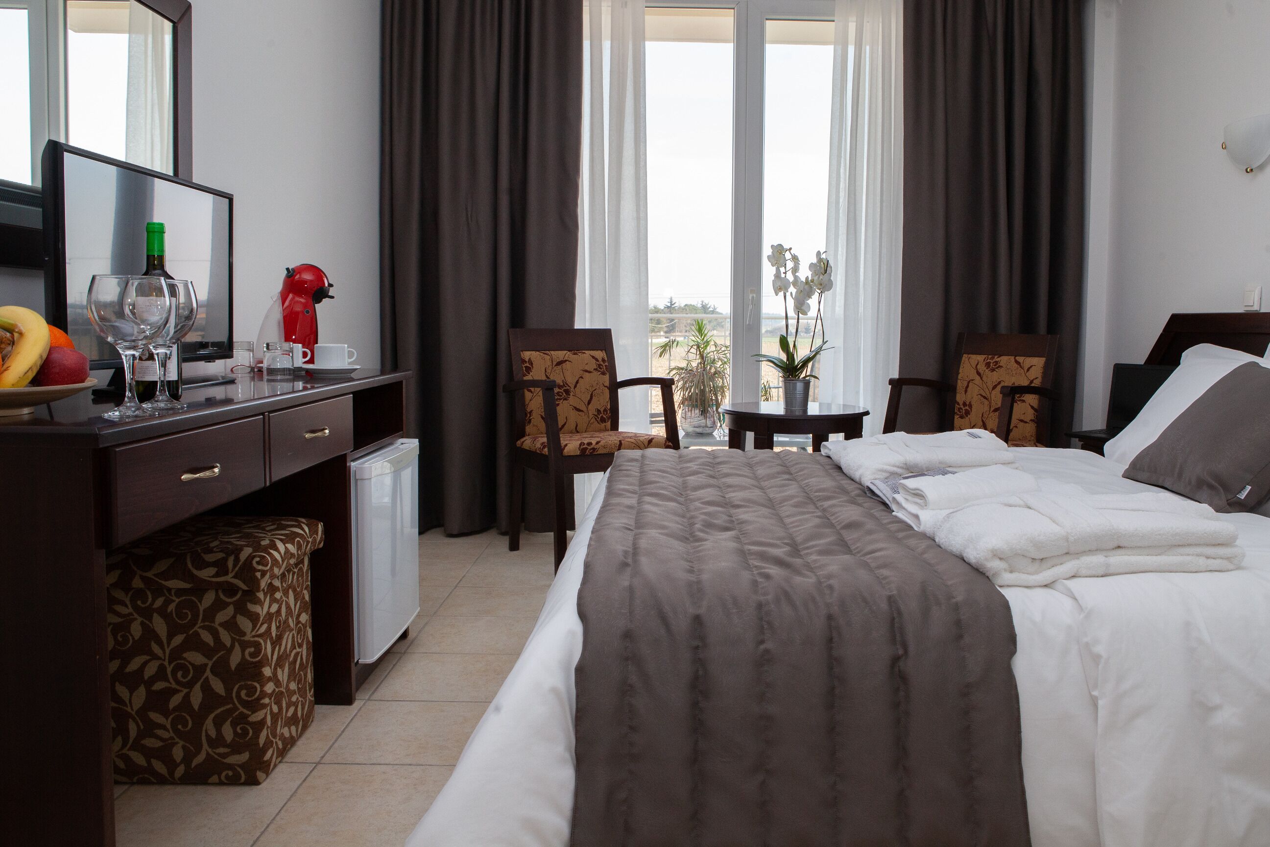 Une chambre d’hôtel avec un lit, un bureau avec un ordinateur, une petite table avec une plante et une vue sur la mer.