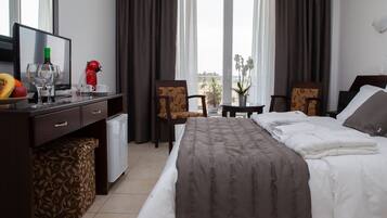 Une chambre d’hôtel avec un lit, un bureau avec un ordinateur, une petite table avec une plante et une vue sur la mer.