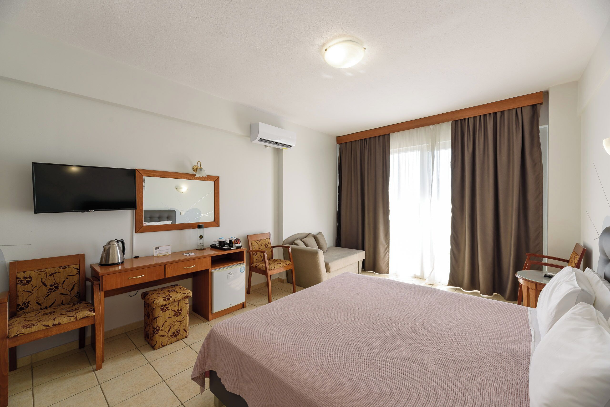 Una habitación de hotel con una cama, un escritorio, una silla, un televisor y una ventana con cortinas.