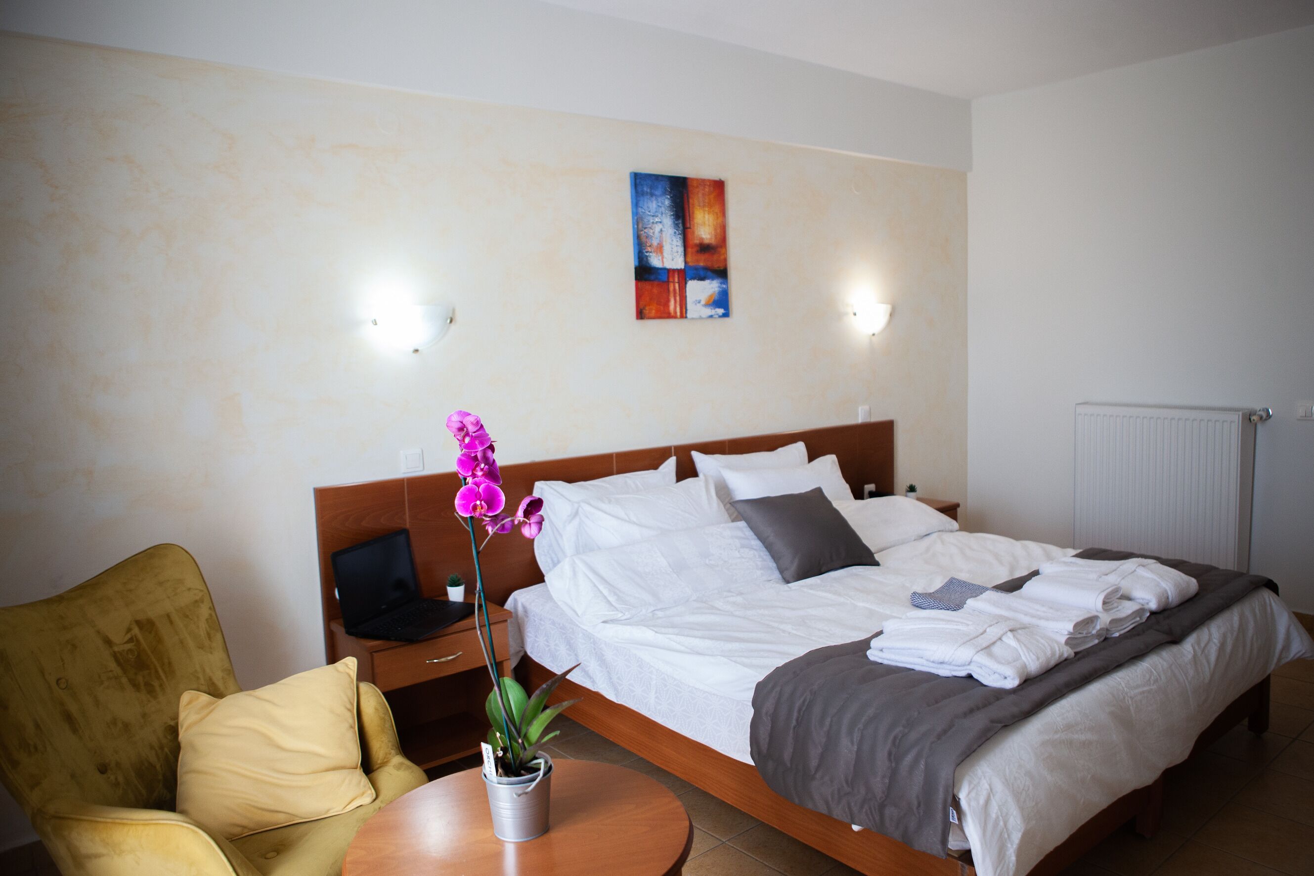 Habitación de hotel con cama, una silla, una mesita con una planta y un cuadro en la pared.