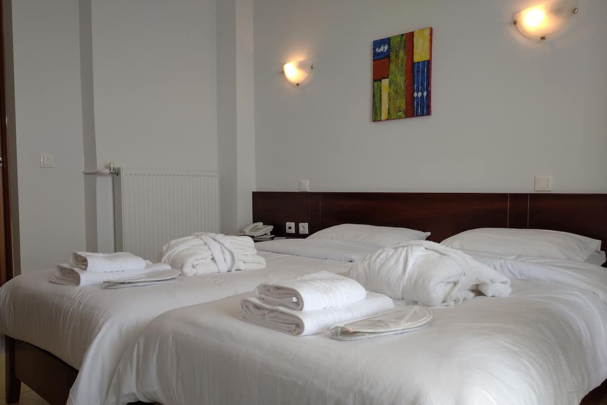 A hotel room with two beds, white linens, towels, a wooden headboard, a radiator, a phone, and a colorful abstract painting on the wall.