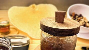 A wooden jar with a lid on a wooden surface, a glass jar with a dark liquid, a bowl of coffee beans, and a yellow cloth.
