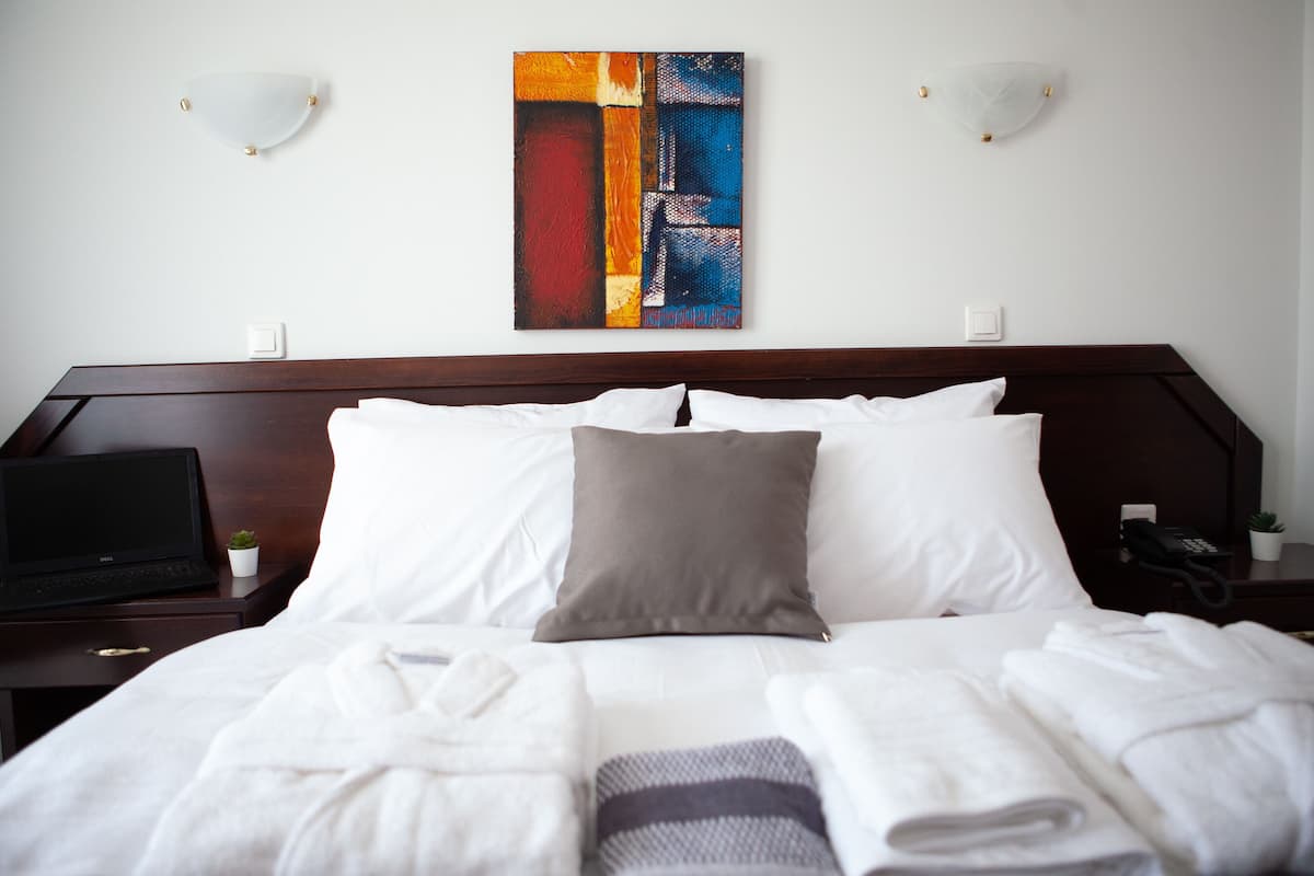 A neatly made bed with white and gray linens, a laptop on a bedside table, and a small potted plant.