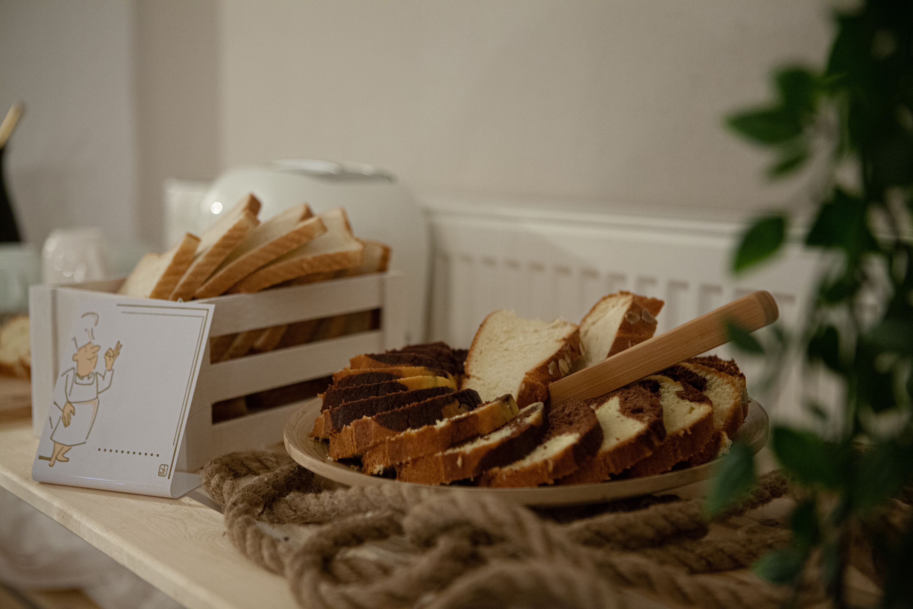 A plate of sliced bread on a table with a toaster and a card featuring a cartoon character.