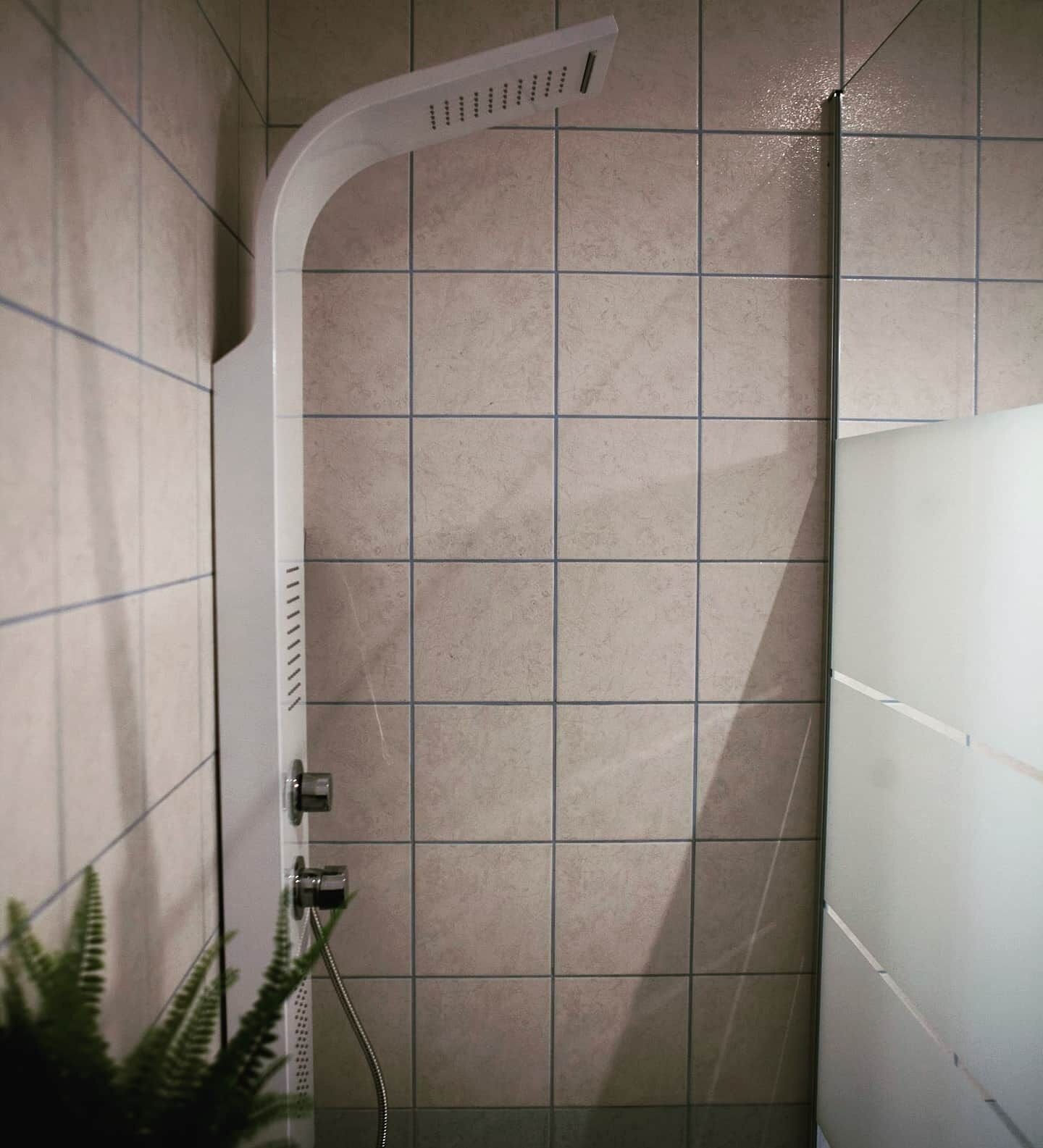A shower with a curved showerhead, tiled walls, and a visible water pipe.
