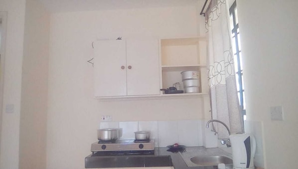 A compact kitchen with a stove, sink, and a small cabinet above the counter.