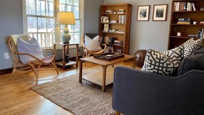 Una sala de estar con suelo de madera, un sofá, una mesa de centro, dos sillones, una estantería y una lámpara.