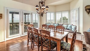 A dining area with a wooden table and chairs, large windows with shutters, and a chandelier. - Oceanfront Escape with Beach Access (Pawleys Island)