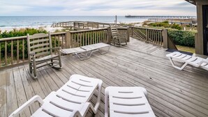 A wooden deck with lounge chairs and a wooden fence overlooking a beach and pier. - Oceanfront Escape with Beach Access (Pawleys Island)