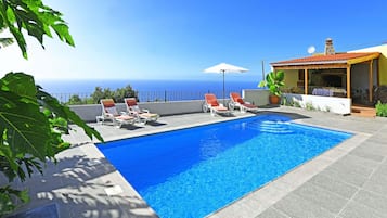 Una piscina con sillones de descanso y vista al océano.
