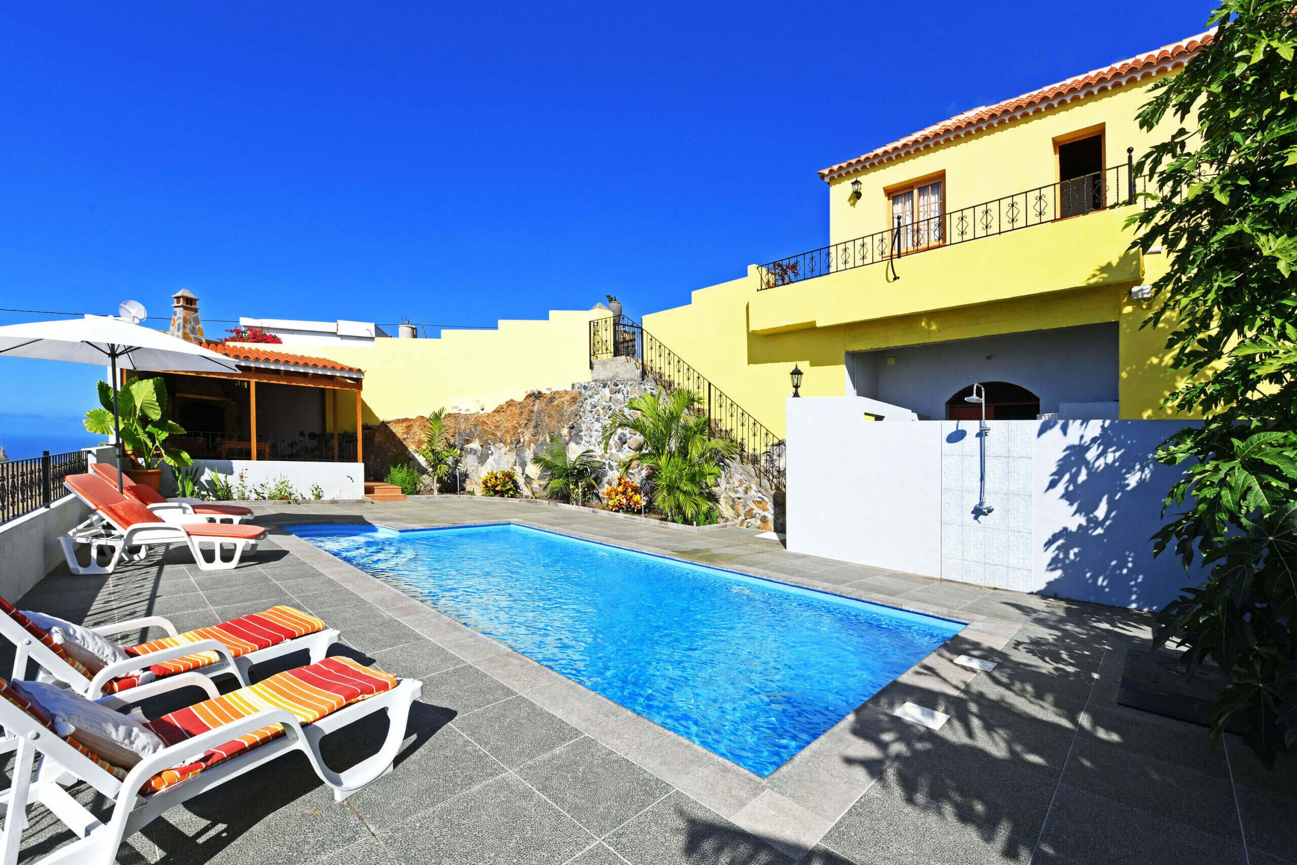 Una piscina amb gandules, un edifici groc amb un balcó i un cel blau clar.