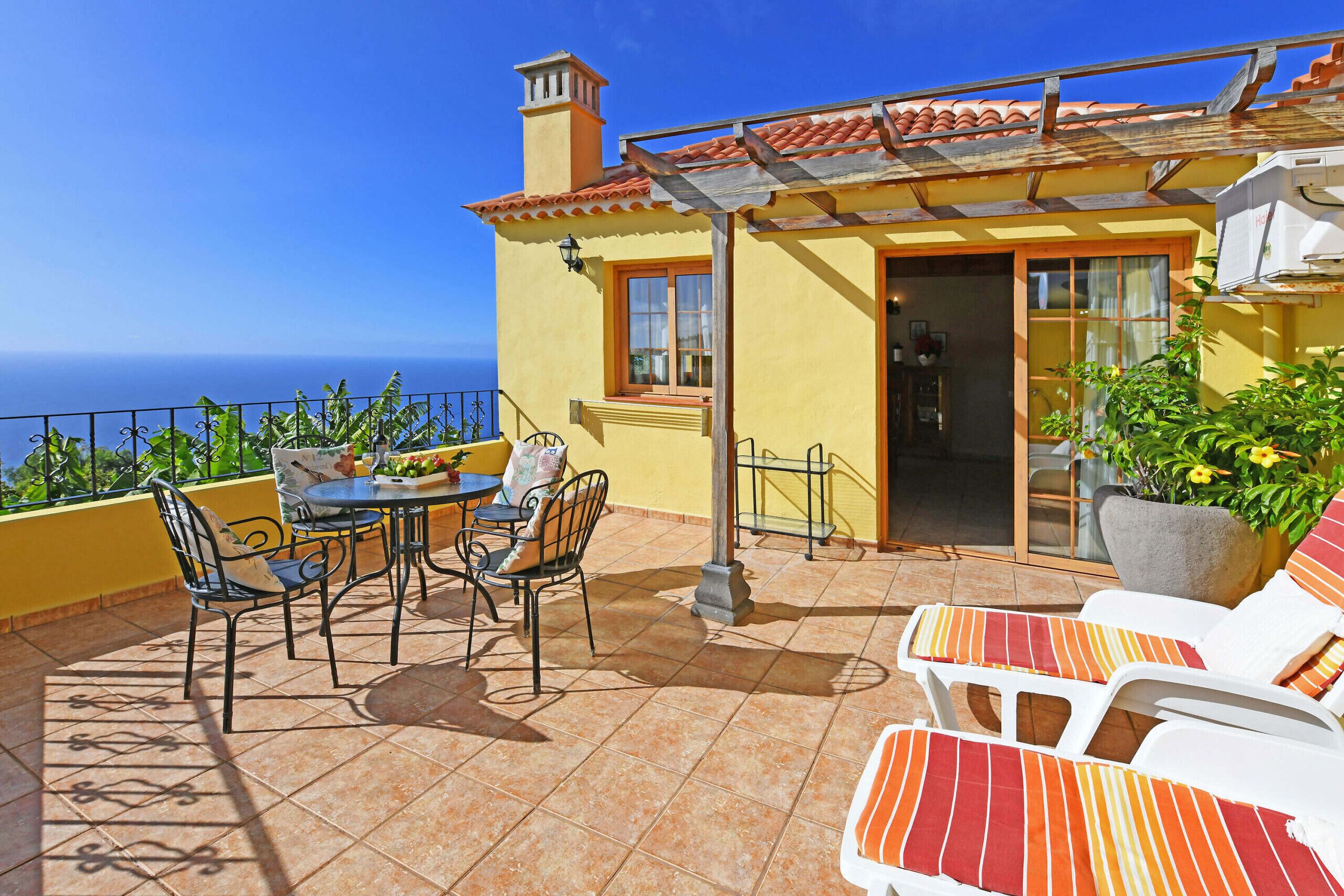 Una terraza con mesa y sillas, una planta en maceta y vista al mar.