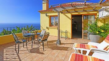 Una terraza con mesa y sillas, una planta en maceta y vista al mar.