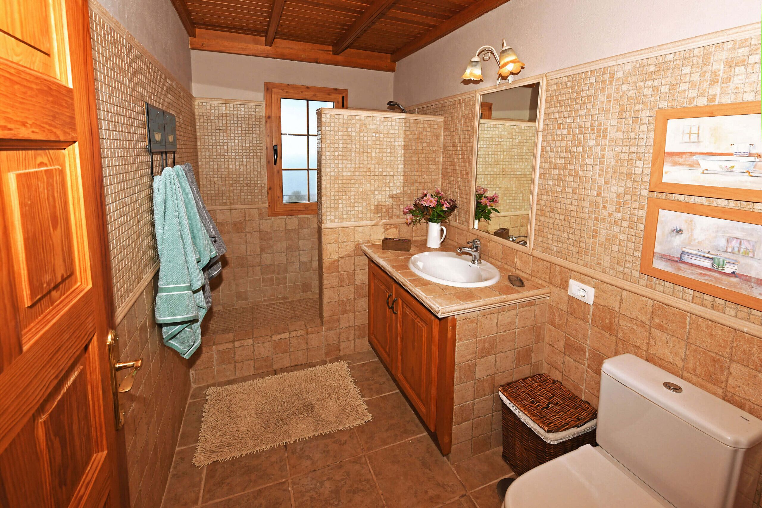 Un baño con tocador de madera, lavamanos, espejo e inodoro.