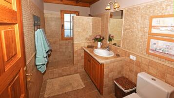 Un baño con tocador de madera, lavamanos, espejo e inodoro.