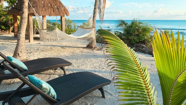 A beach setting with a thatched hut, a hammock, and lounge chairs with cushions. - Beachfront CASA PAAMUL Riviera Maya-Tulum (Paamul)
