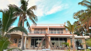 A two-story building with a balcony, large windows, and a sandy courtyard surrounded by palm trees. - Beachfront CASA PAAMUL Riviera Maya-Tulum (Paamul)