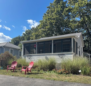 A single-story building with a large windowed front section, two red Adirondack chairs in front, and a small garden area with various plants and flowers. - Unbeatable location! Walk to beach and town. (Ogunquit)