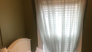 A bedroom with a bed, white pillows, a bedside table with a lamp, and sheer curtains on a window. - Unbeatable location! Walk to beach and town. (Ogunquit)