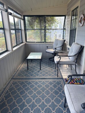 A covered porch with two chairs, a small table, and a patterned rug.